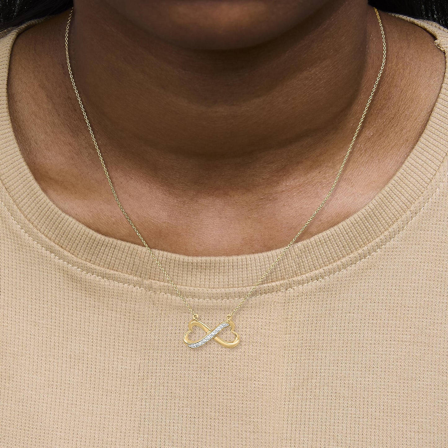Yellow metal infinity-shaped necklace with a pave setting of white round gemstones on one side, shown worn on a model, front-facing angle.