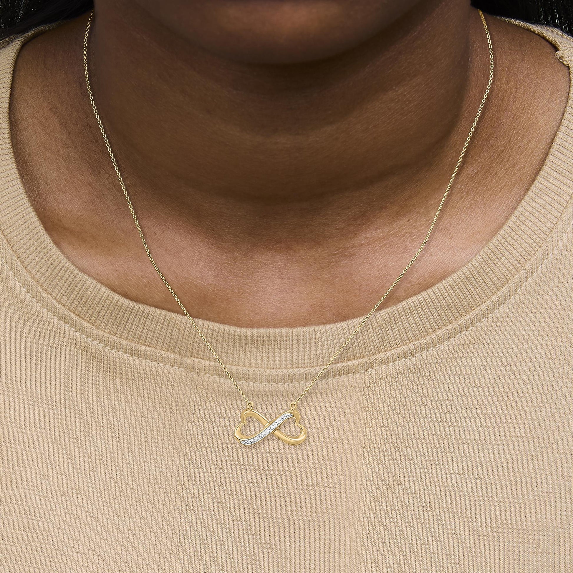 Yellow metal infinity-shaped necklace with a pave setting of white round gemstones on one side, shown worn on a model, front-facing angle.