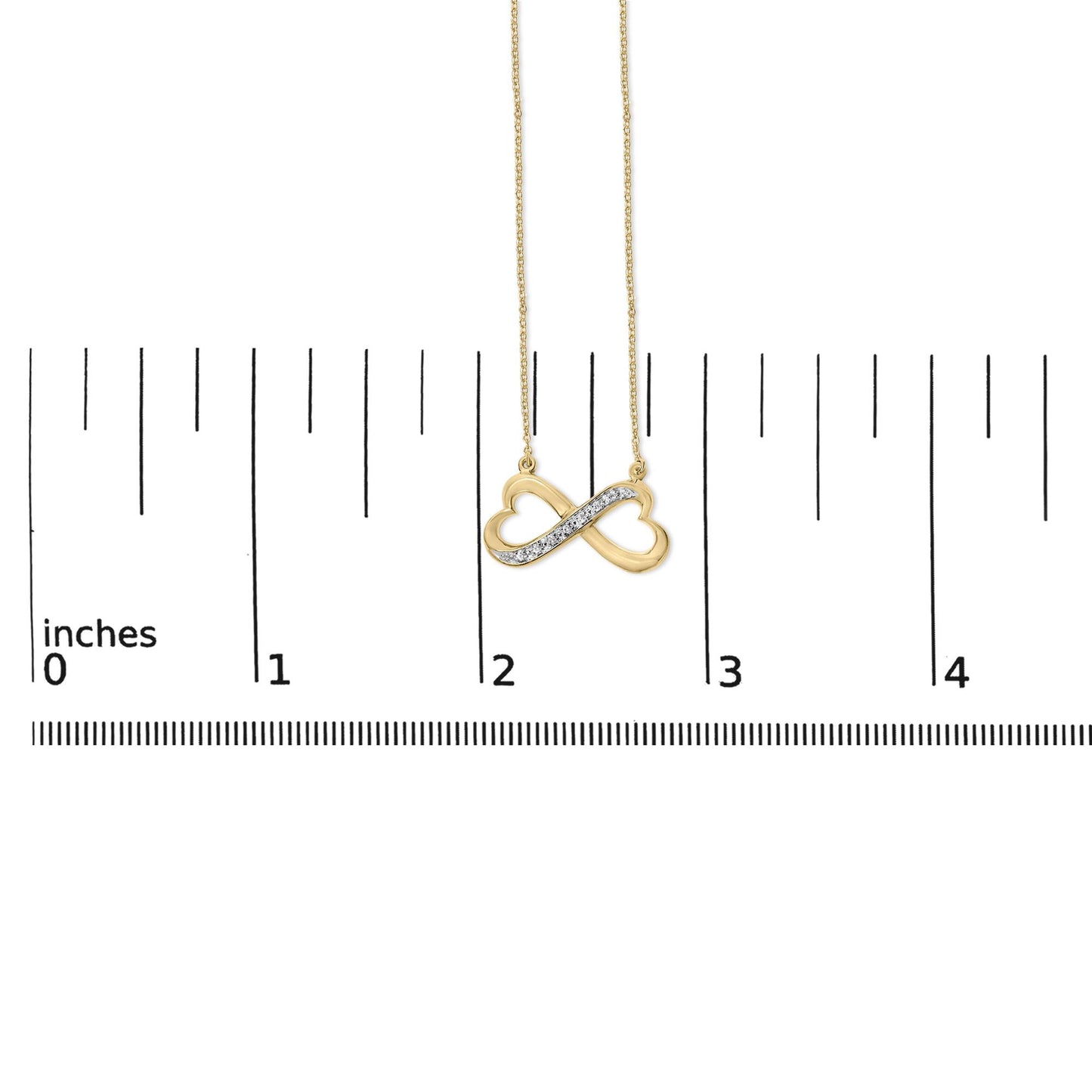 Close-up front view of a yellow metal infinity necklace pendant with two heart shapes and a diagonal row of white gemstones in pave setting, shown on a measurement scale.