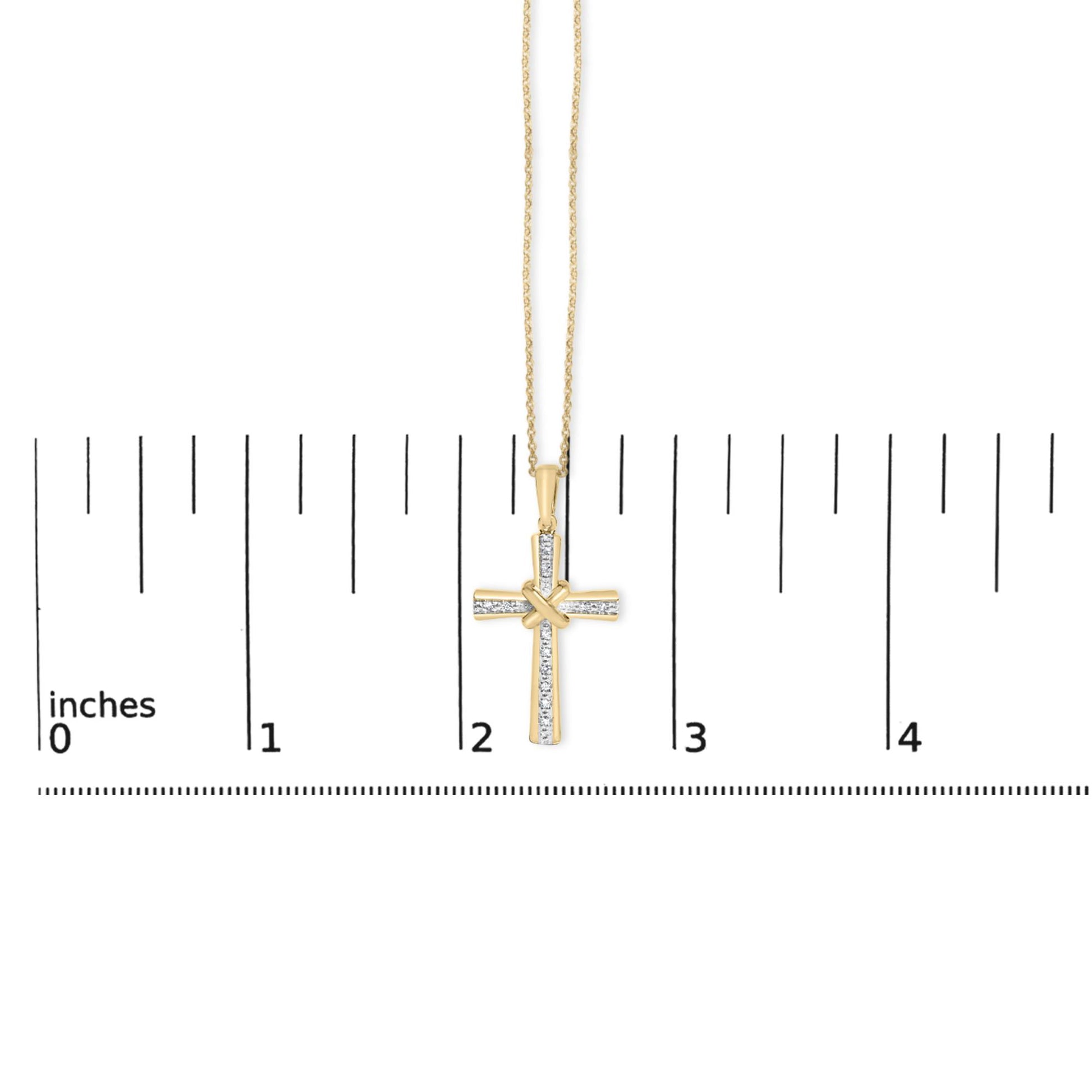 Close-up front view of a yellow necklace with a cross pendant featuring white gemstones in a pave setting, shown on a scale with inch markings.