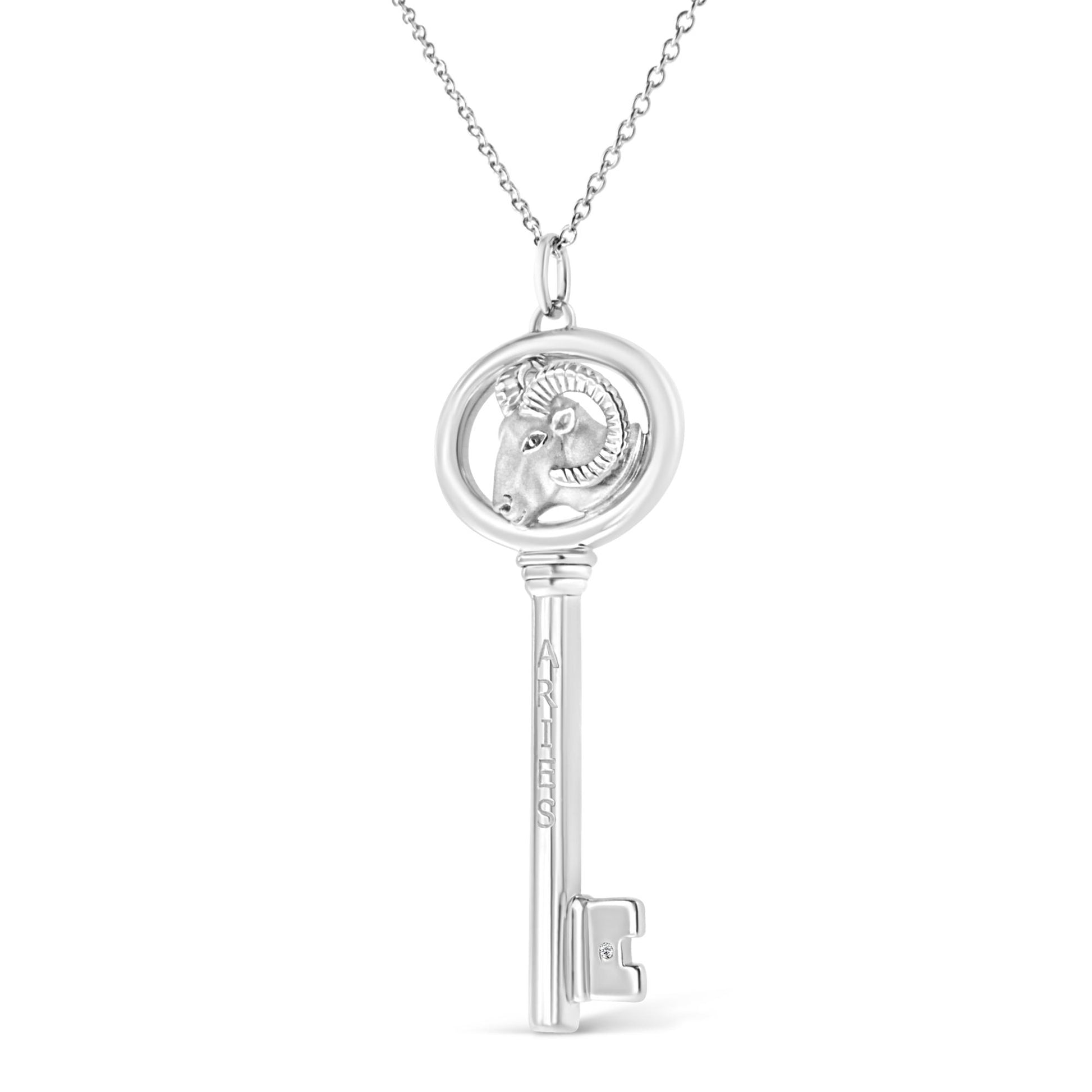 Front-facing shot of a white metal necklace pendant shaped like a key, featuring a ram's head inside a circular frame at the top and labeled 'ARIES' on the shaft, with a small round brownish gemstone in a bezel setting near the key's teeth.