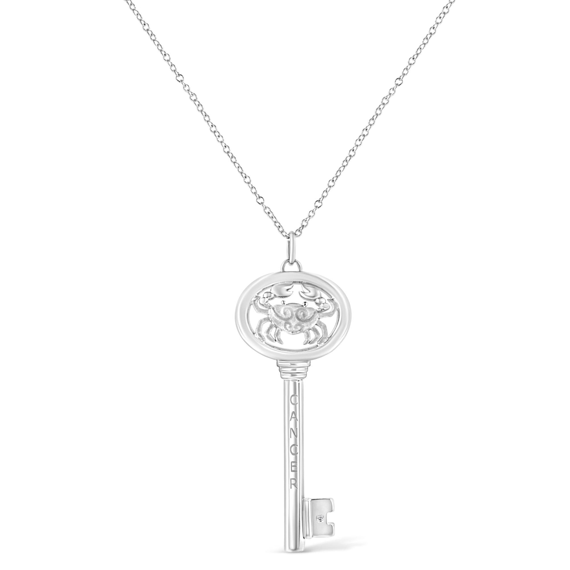 Front view of a white metal key-shaped necklace pendant with a crab design at the top oval section and a round brownish bezel-set gemstone near the bottom.