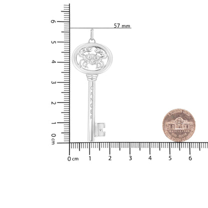 White metal necklace pendant in the shape of a key with a crab design at the top and an engraved word on the shaft, featuring a single round brownish gemstone in bezel setting near the bottom, photographed flat on a ruler and scale for size reference from a top-down angle.