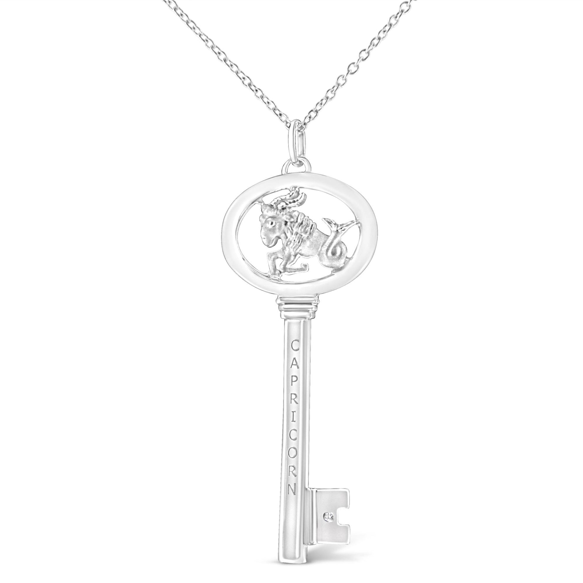 Front view of white metal key-shaped necklace pendant with Capricorn symbol and engraved text, featuring one round brownish bezel-set gemstone.