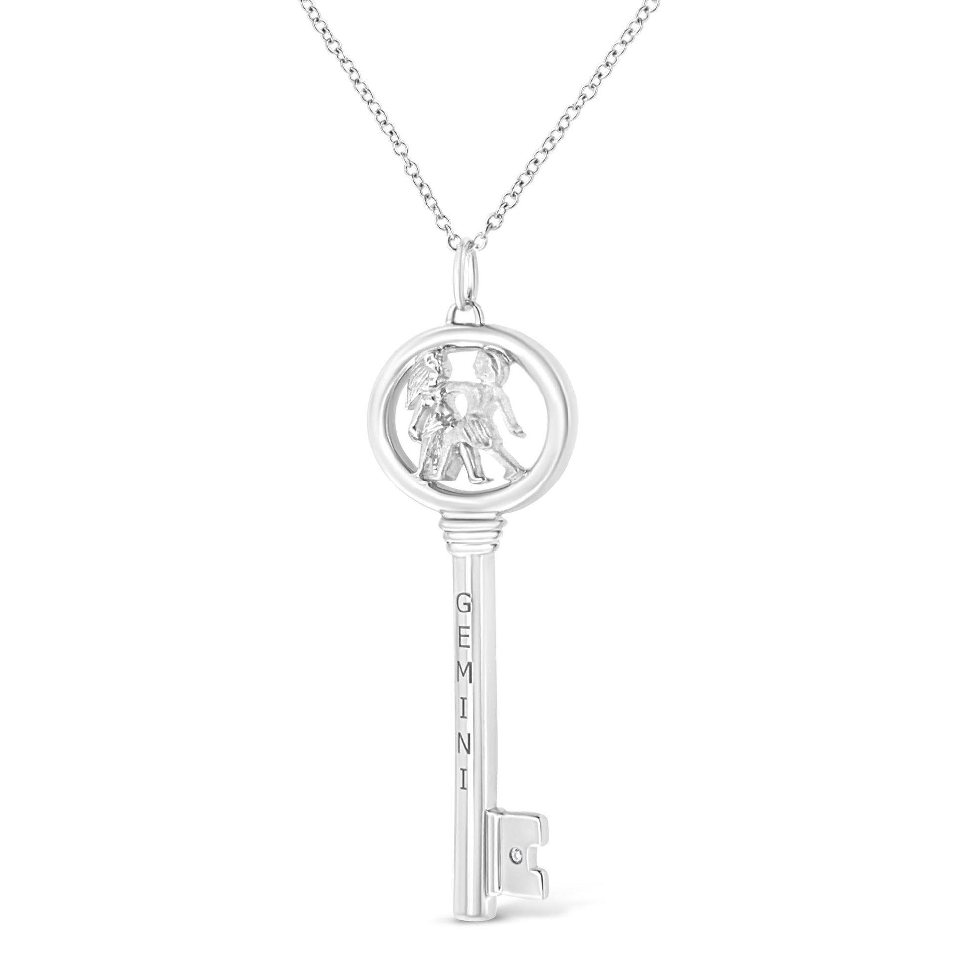 Front view of a white metal key-shaped necklace pendant with figures inside a circular top, engraved with 'GEMINI' on the shaft, and a round brownish gemstone in a bezel setting near the bottom.