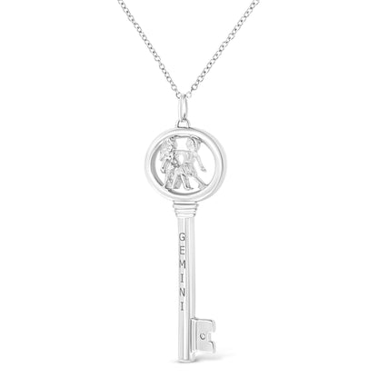 Front view of a white metal key-shaped necklace pendant with figures inside a circular top, engraved with 'GEMINI' on the shaft, and a round brownish gemstone in a bezel setting near the bottom.