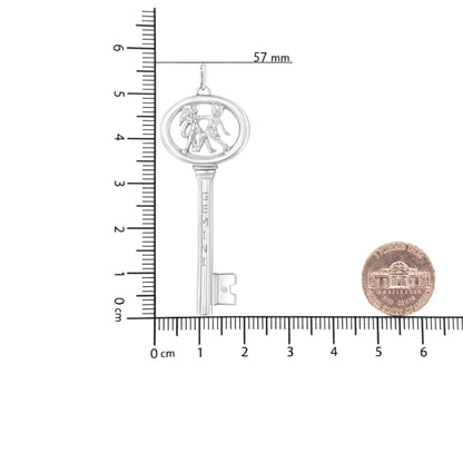 White necklace pendant in key shape with two figures inside the top oval, one with wings, the word 'GEMINI' on the shaft, and a round brownish gemstone in bezel setting near the teeth, shot from the front on a ruler for size reference with a coin nearby.