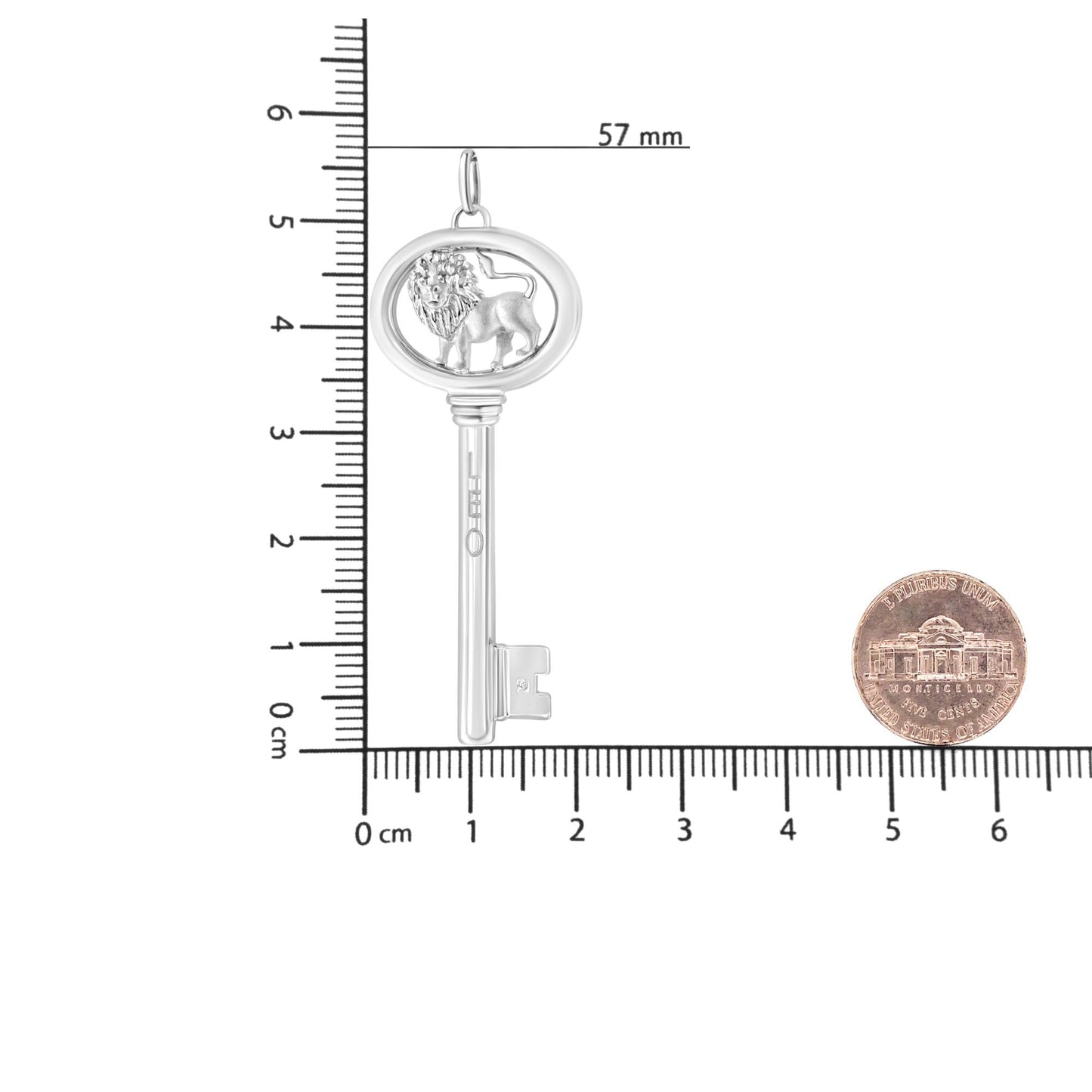 Top-down view of a white metal key-shaped necklace pendant with a lion design inside the oval top, featuring one round brownish gemstone in a bezel setting, placed on a ruler and scale with a coin for size reference.