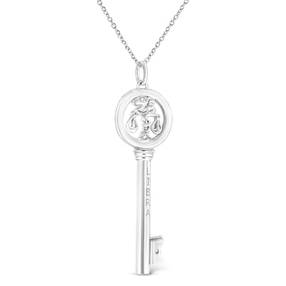 Front view of a white metal key-shaped necklace pendant with a Libra symbol inside the circular top and a single brownish round gemstone in bezel setting near the bottom end, hanging from a chain.