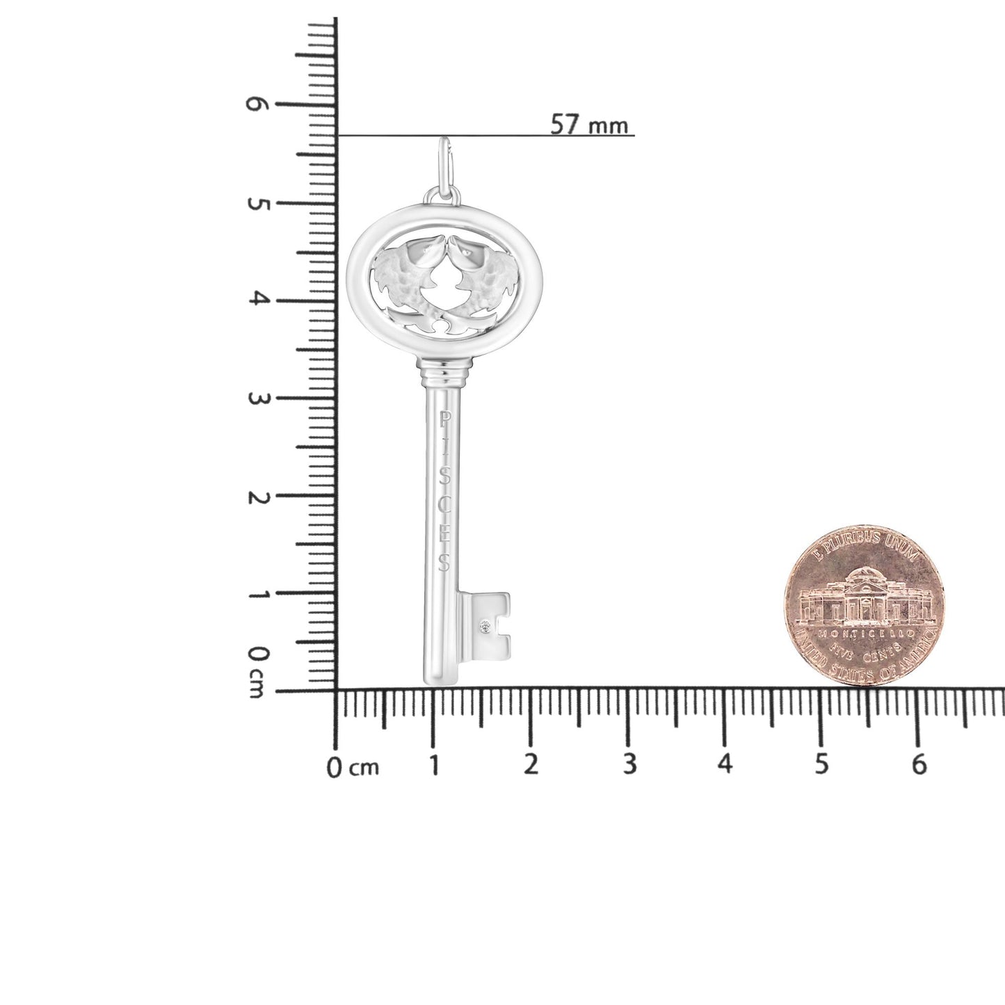 Top-down view of white necklace pendant in the shape of a key with a round bezel-set brownish gemstone near the base, placed on a ruler for size reference.