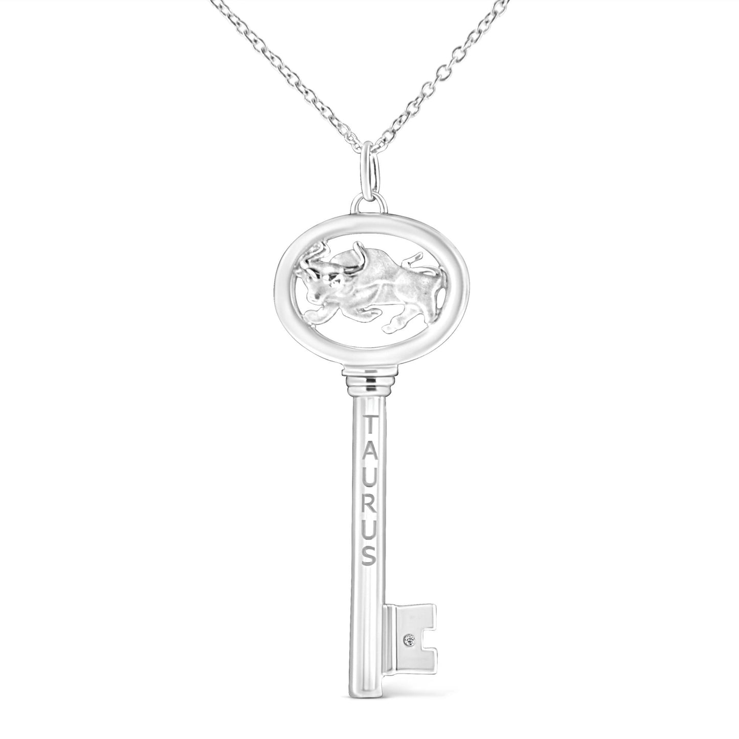Front-facing shot of a white metal key-shaped necklace pendant with a bull motif in the oval top and the word 'TAURUS' vertically engraved on the shaft, featuring a round brownish bezel-set gemstone near the key bit.