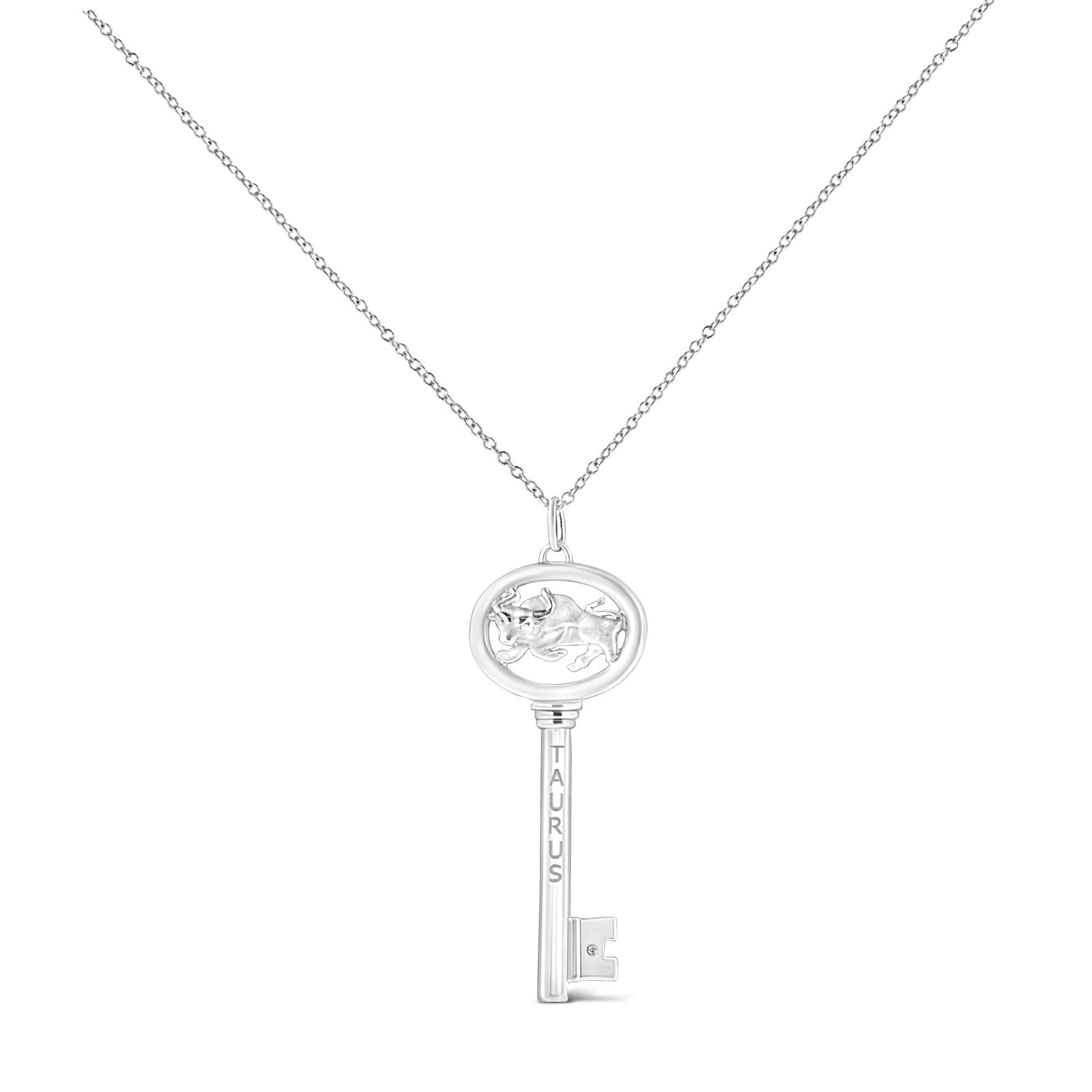 White metal key-shaped necklace pendant with an oval top featuring a raised bull figure and engraved 'TAURUS' on the shaft, with a small brownish round gemstone set near the key bit, shown in a front-facing view.