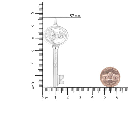 White metal key-shaped necklace pendant with an oval top featuring a profile of a woman and a round brownish gemstone set in bezel near the bottom, photographed flat on a ruler for size reference from a top-down angle.