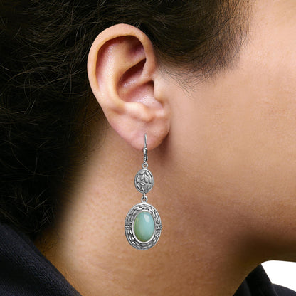 White metal dangle earring with an oval gray gemstone in a bezel setting framed by white round gemstones in a prong setting. Shown worn on a model from a side angle.