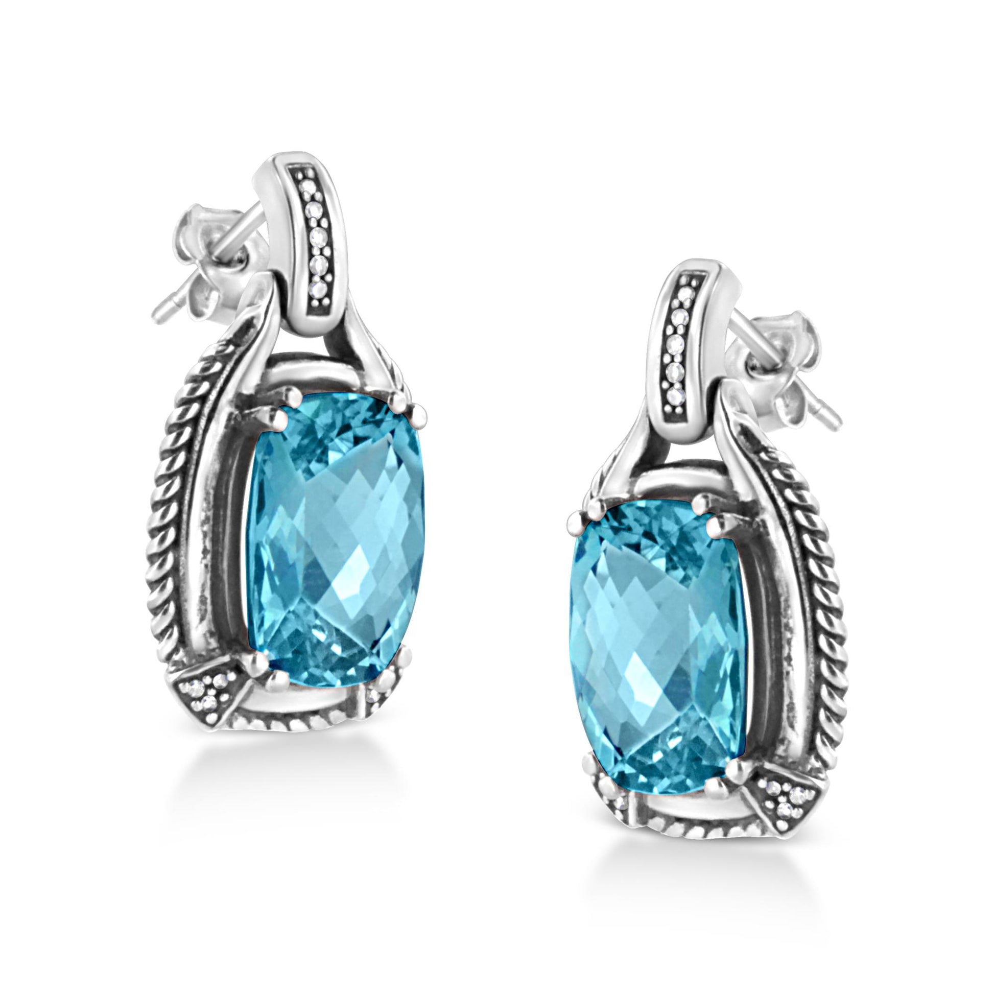 Pair of white metal earrings shown at a slight angle, each featuring a cushion-shaped blue gemstone in prong setting surrounded by small round white gemstones in invisible setting.