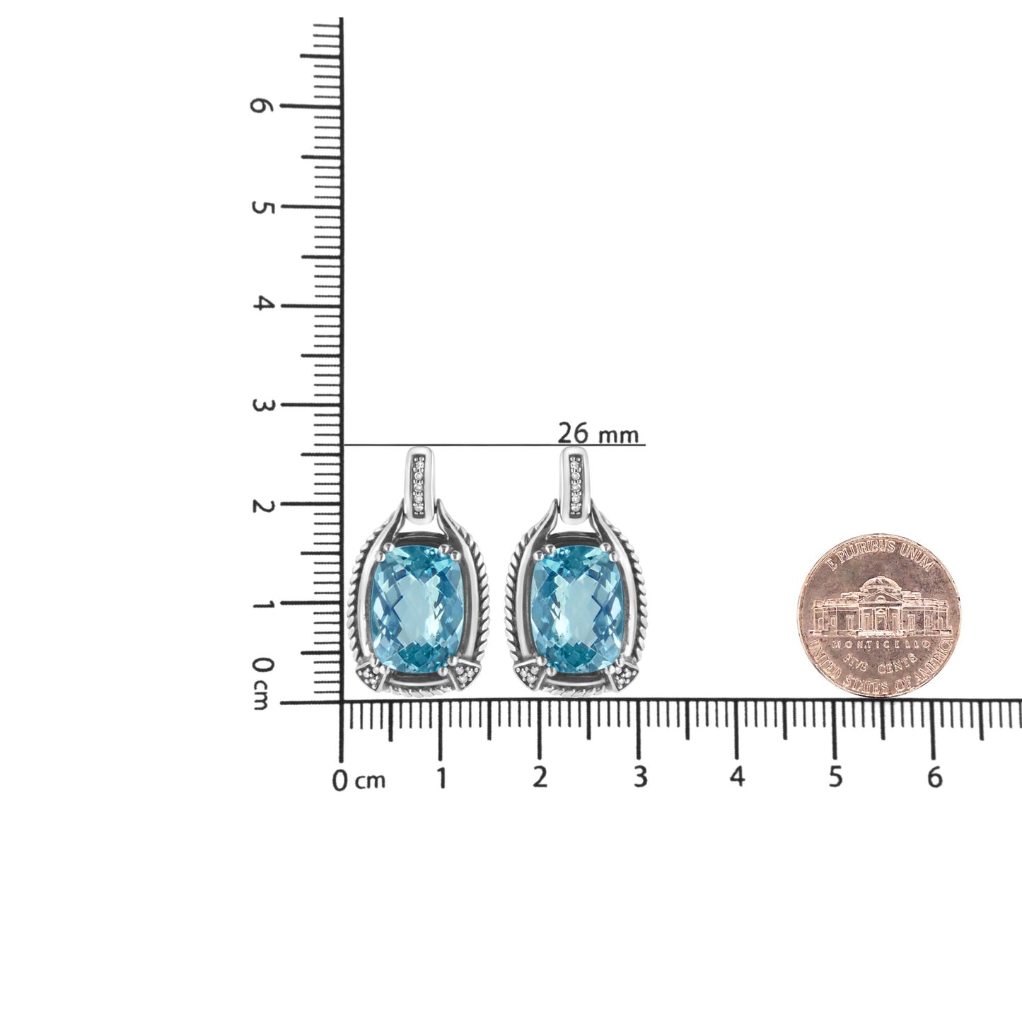 Pair of white metal earrings with cushion-shaped blue gemstones and round white gemstones, shown from the front on a ruler and next to a coin for size reference.