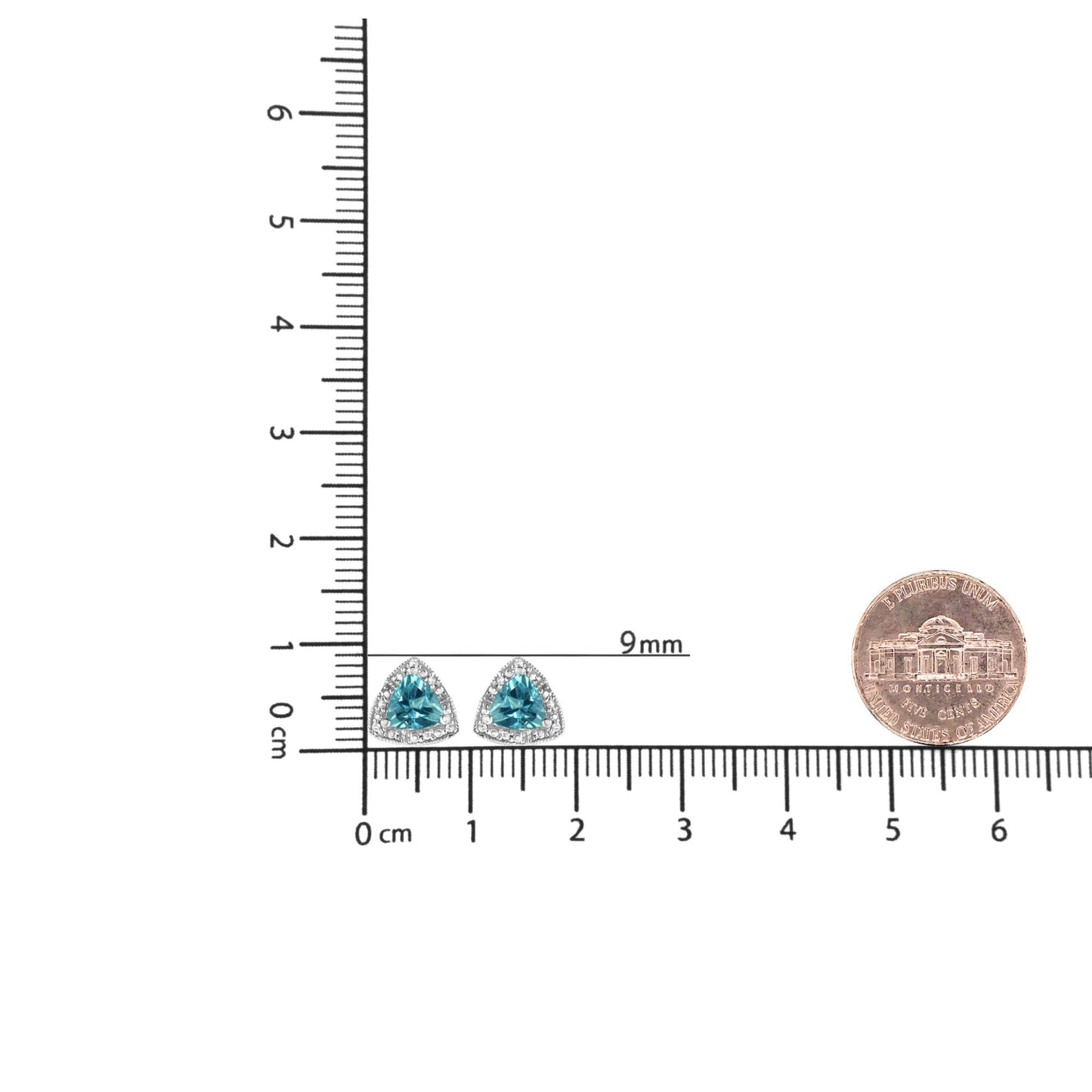 Front angle close-up of white metal earrings with blue trillion-shaped gemstones surrounded by round white gemstones, displayed on a ruler with a coin for size reference.