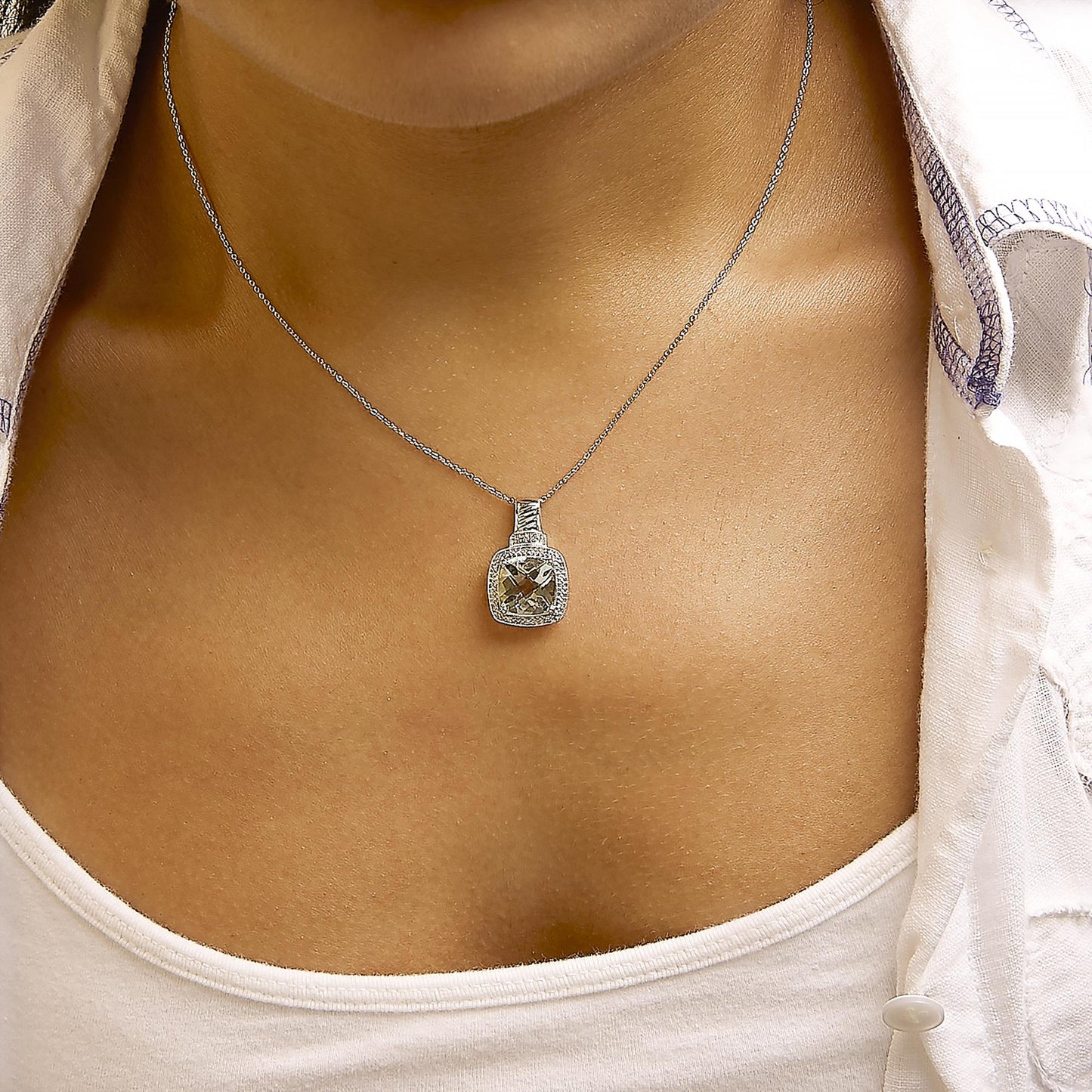 White necklace with a cushion-shaped green gemstone pendant surrounded by a pave setting of white gemstones, shown worn on a model in a close-up front angle.
