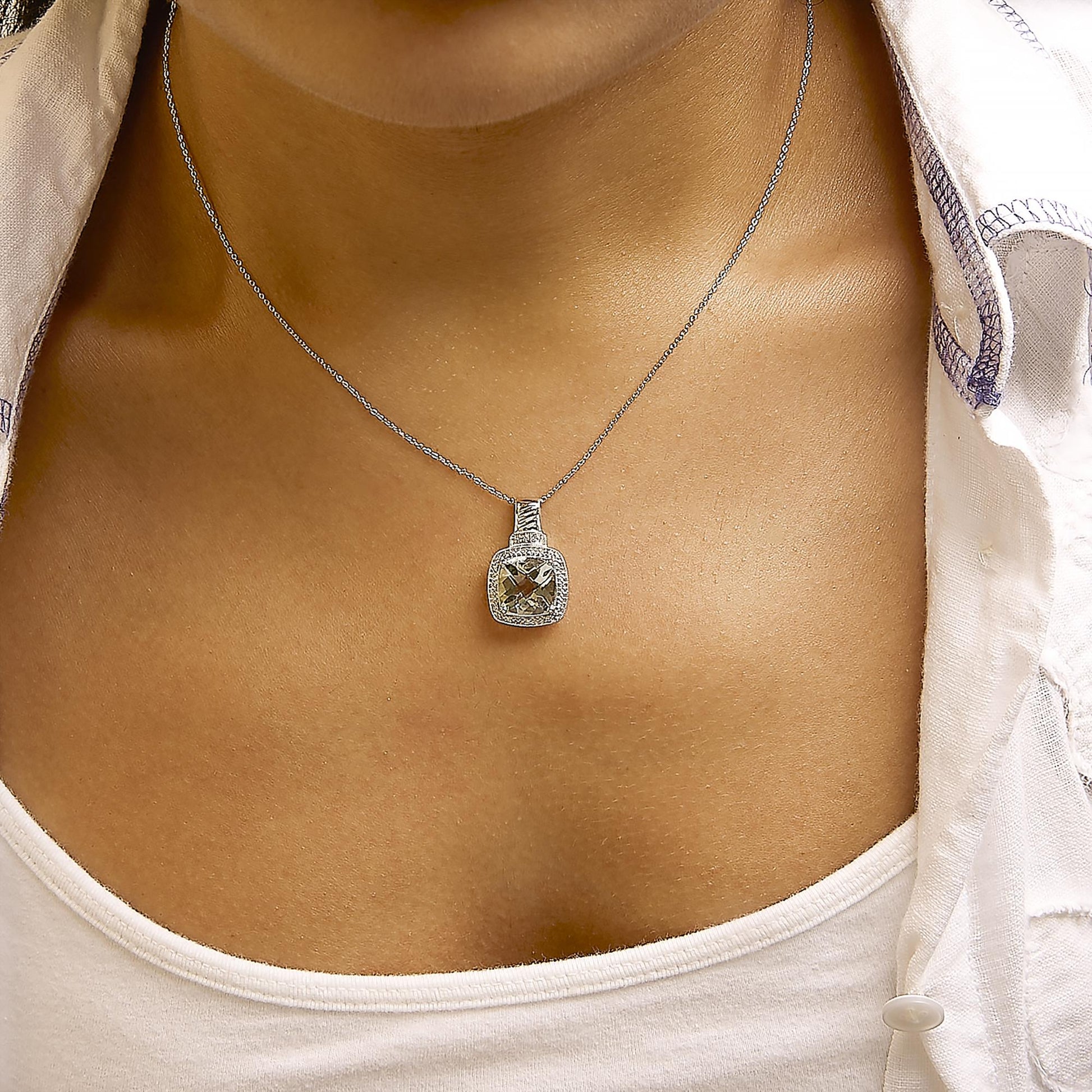 White necklace with a cushion-shaped green gemstone pendant surrounded by a pave setting of white gemstones, shown worn on a model in a close-up front angle.