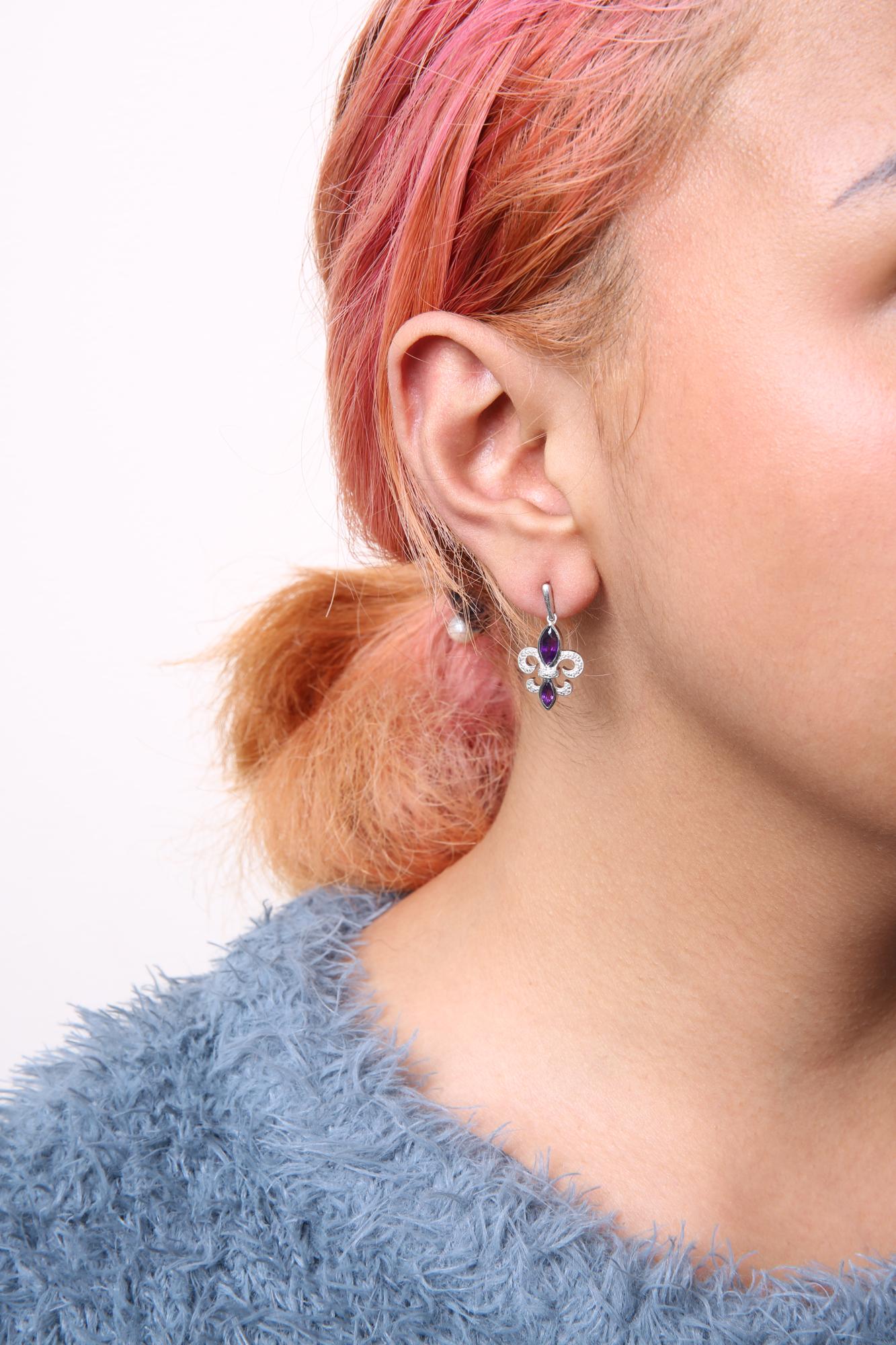 Close-up side view of a model wearing white metal earrings featuring two purple gemstones and multiple small white round gemstones in prong settings.