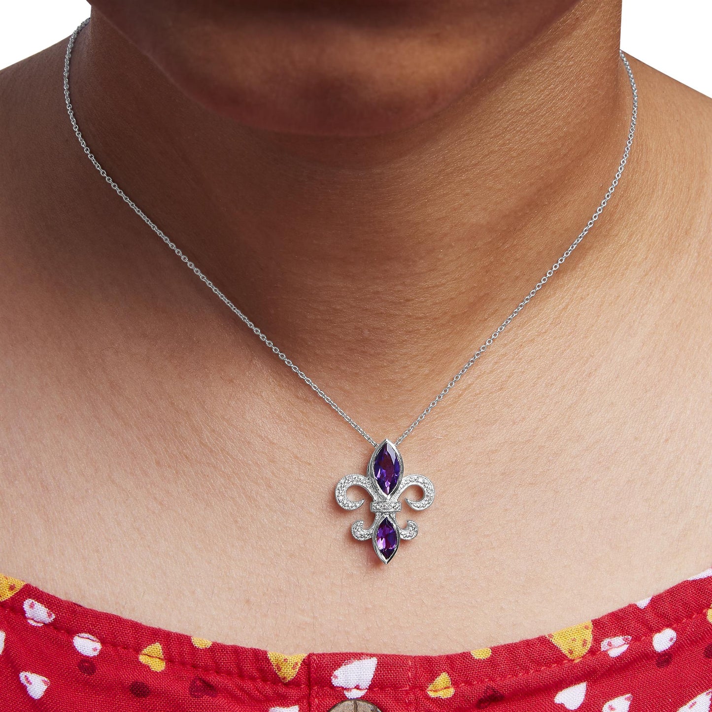 Close-up front view of a white necklace on a model featuring a fleur-de-lis pendant with two marquise-shaped purple gemstones in bezel settings and surrounded by round white gemstones in prong settings.