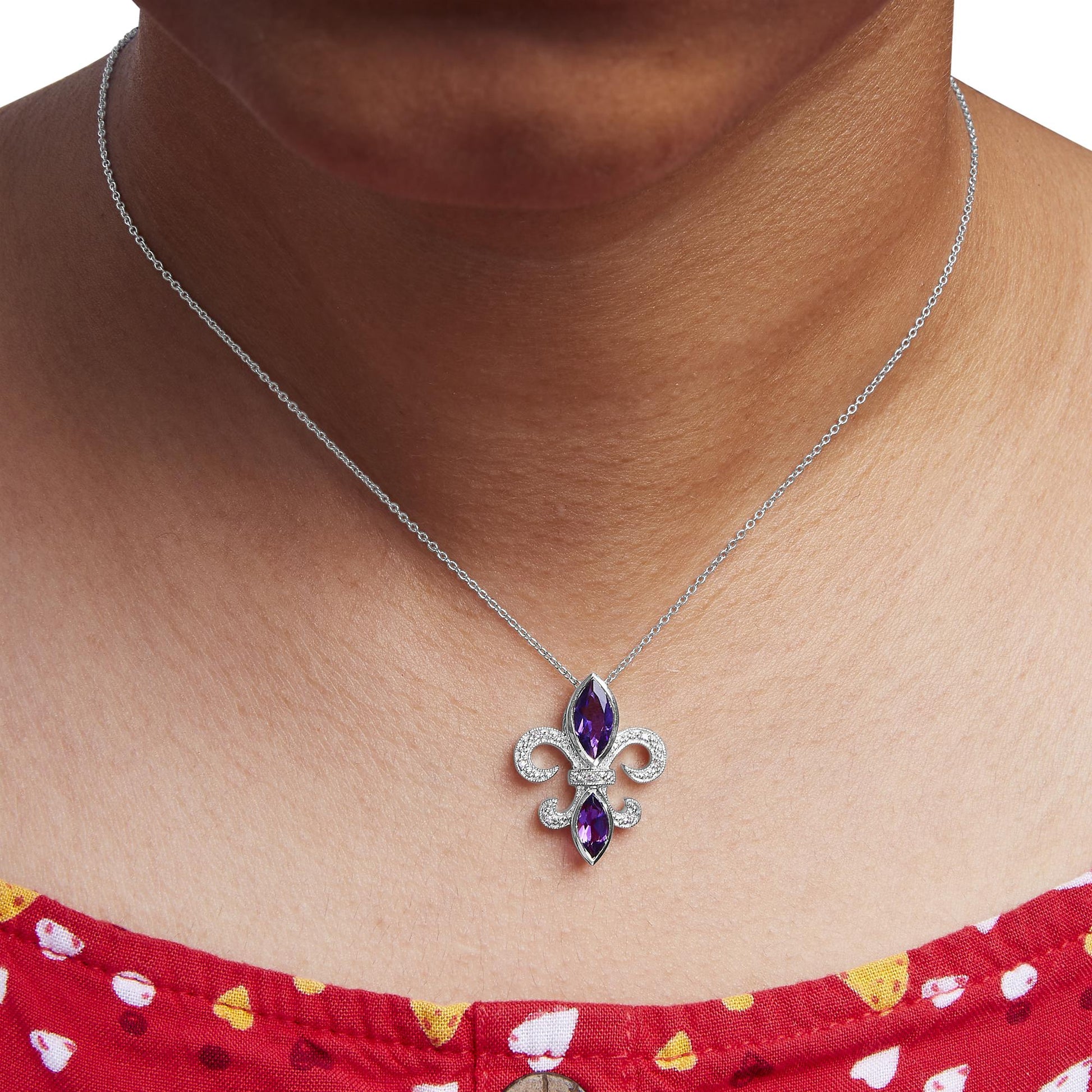 Close-up front view of a white necklace on a model featuring a fleur-de-lis pendant with two marquise-shaped purple gemstones in bezel settings and surrounded by round white gemstones in prong settings.