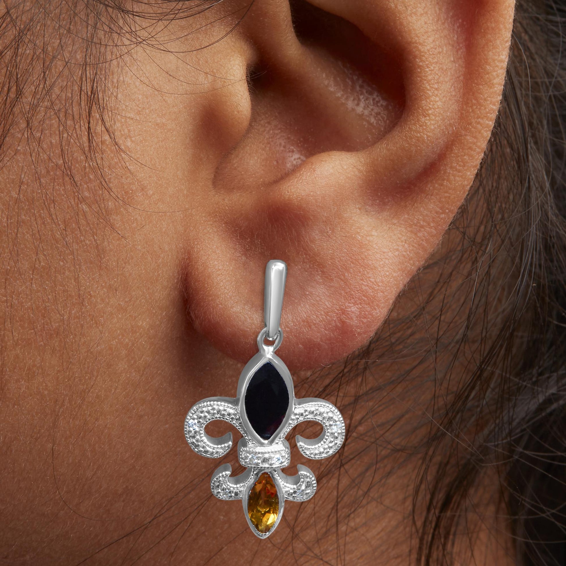 Close-up front view of a white metal earring on a model's ear featuring an ornate design with one black marquise-shaped gemstone in a bezel setting, one yellow marquise-shaped gemstone in a bezel setting, and small round white gemstones in prong settings decorating the piece.