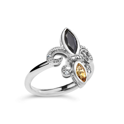 White metal ring with a fleur-de-lis design viewed at an angle, featuring a marquise-shaped black gemstone, a marquise-shaped orange gemstone in bezel setting, and small white round gemstones in pave setting.