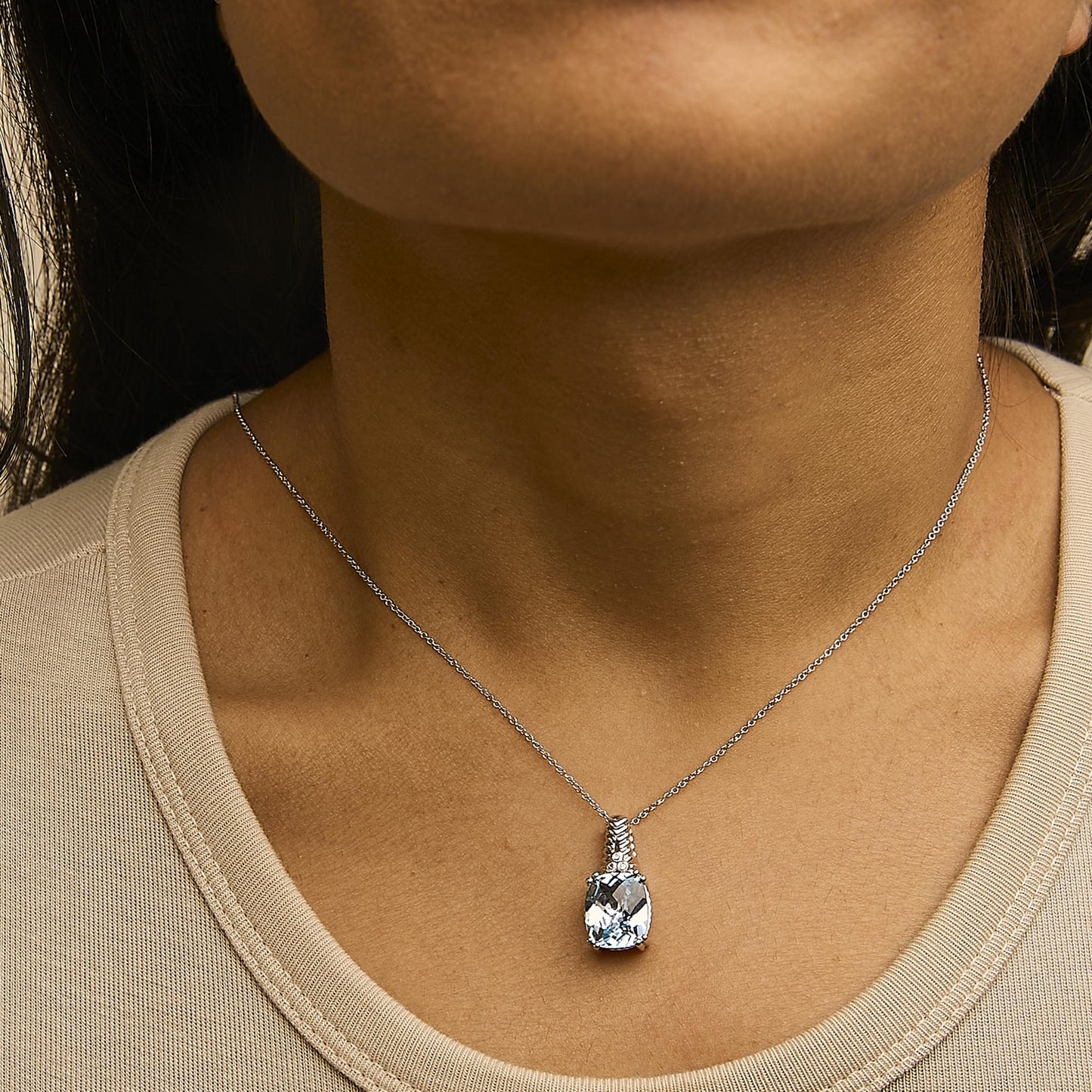 Necklace with a cushion-shaped blue gemstone pendant and three small round white gemstones above it, shown worn on a model from a front angle.