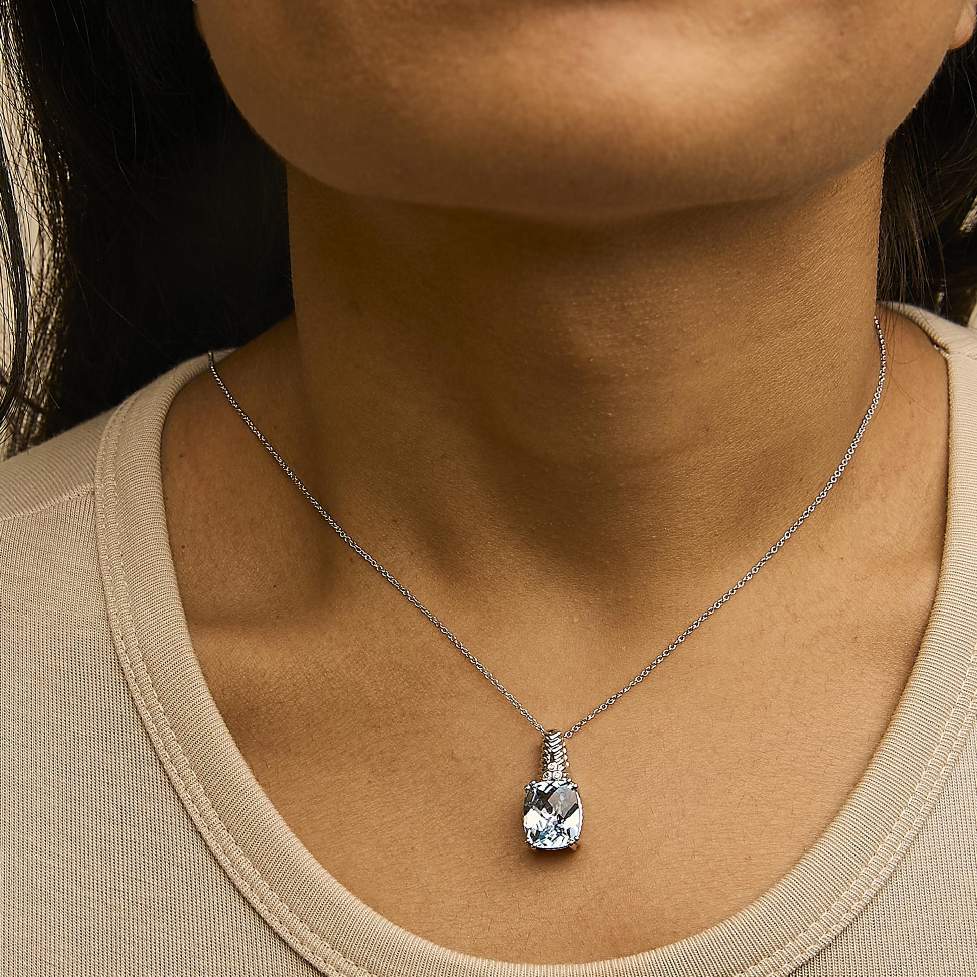 Necklace with a cushion-shaped blue gemstone pendant and three small round white gemstones above it, shown worn on a model from a front angle.