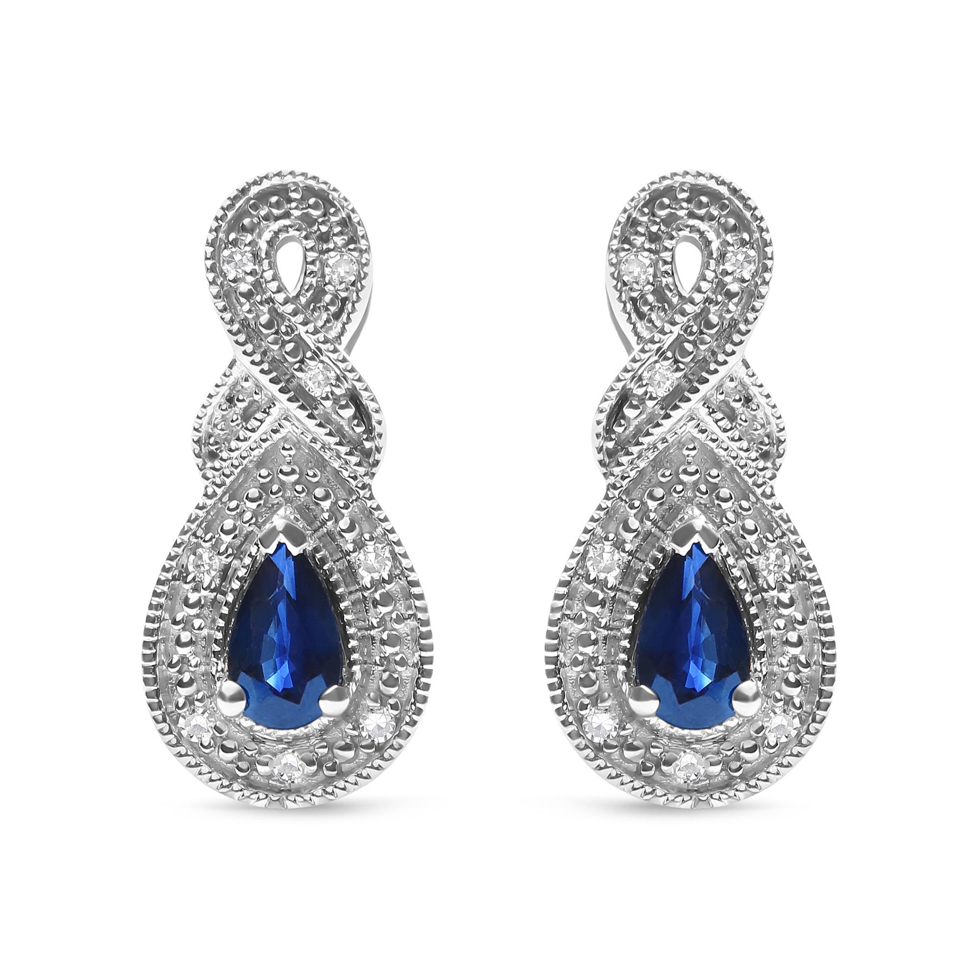 Front-facing close-up of white metal earrings featuring pear-shaped blue gemstones surrounded by round white gemstones in a prong setting, with an intertwined design above the gemstones.