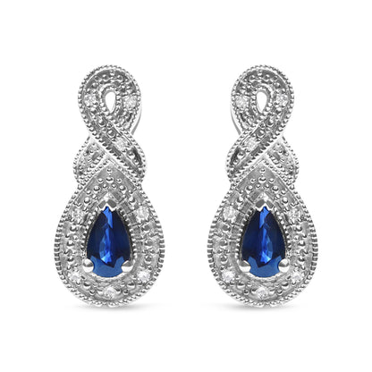 Front-facing close-up of white metal earrings featuring pear-shaped blue gemstones surrounded by round white gemstones in a prong setting, with an intertwined design above the gemstones.