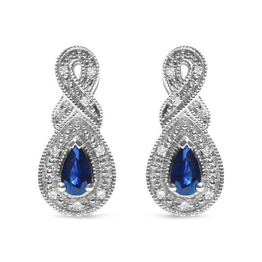 Front-facing close-up of white metal earrings featuring pear-shaped blue gemstones surrounded by round white gemstones in a prong setting, with an intertwined design above the gemstones.