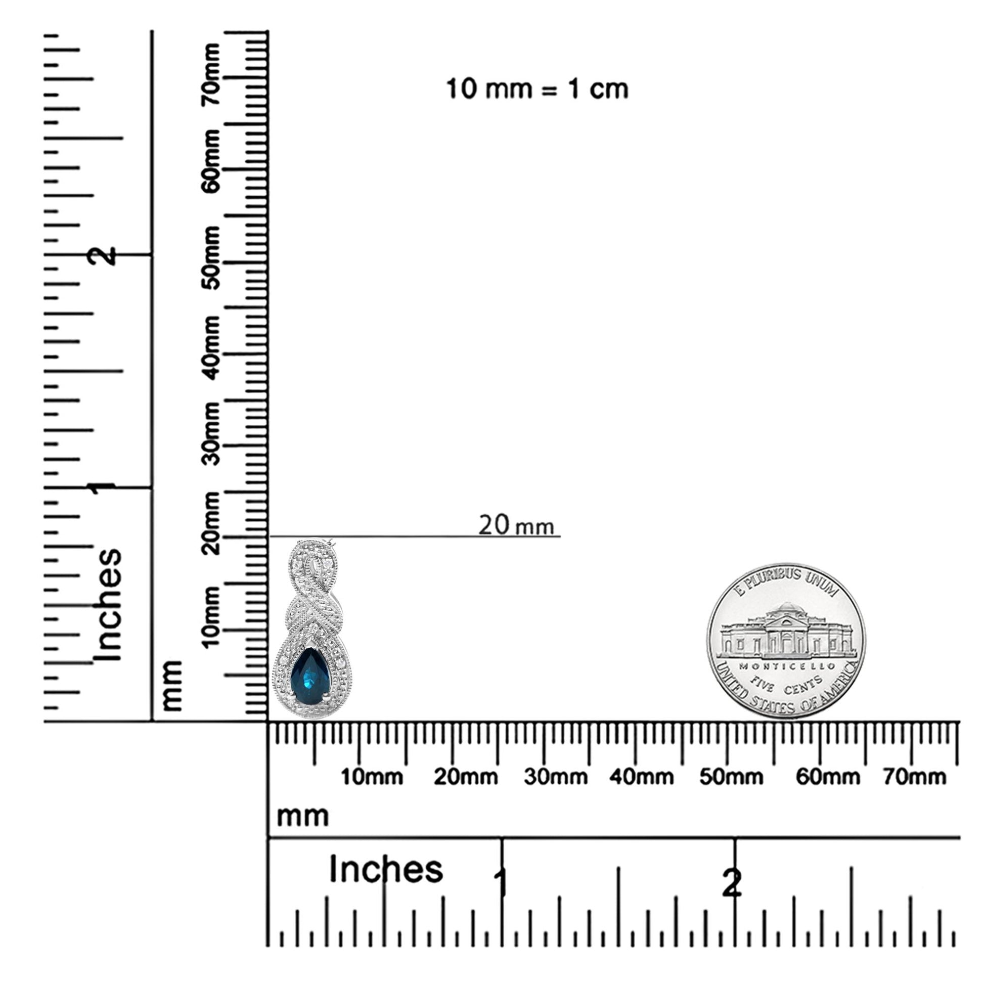 White necklace pendant with a pear-shaped blue gemstone surrounded by round white gemstones, prong set, shown on a ruler and scale for size reference, front angle.