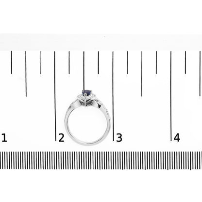 White metal ring with a pear-shaped blue gemstone and round white gemstones in prong settings, shown from a top angle on a ruler for size reference.