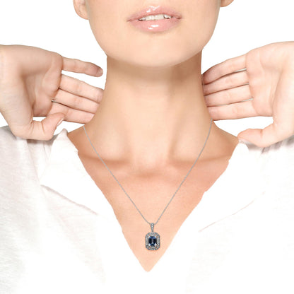White metal necklace with a rectangular blue gemstone pendant surrounded by multiple round white gemstones, shown on a model from the front.