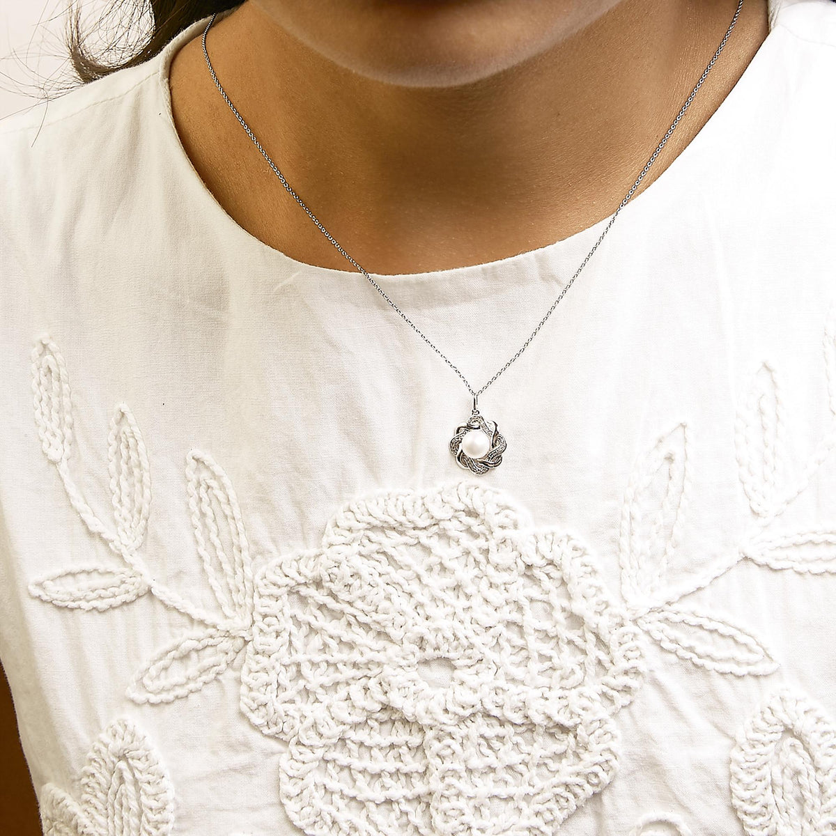 Close-up front view of a model wearing a white metal necklace with a pendant featuring a central white gemstone surrounded by an intertwined design accented with white gemstones in prong settings.