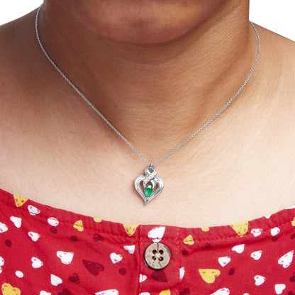 White metal heart-shaped necklace with a pear-shaped green gemstone in the center and four round white gemstones along the top, shown on a model from a front angle.