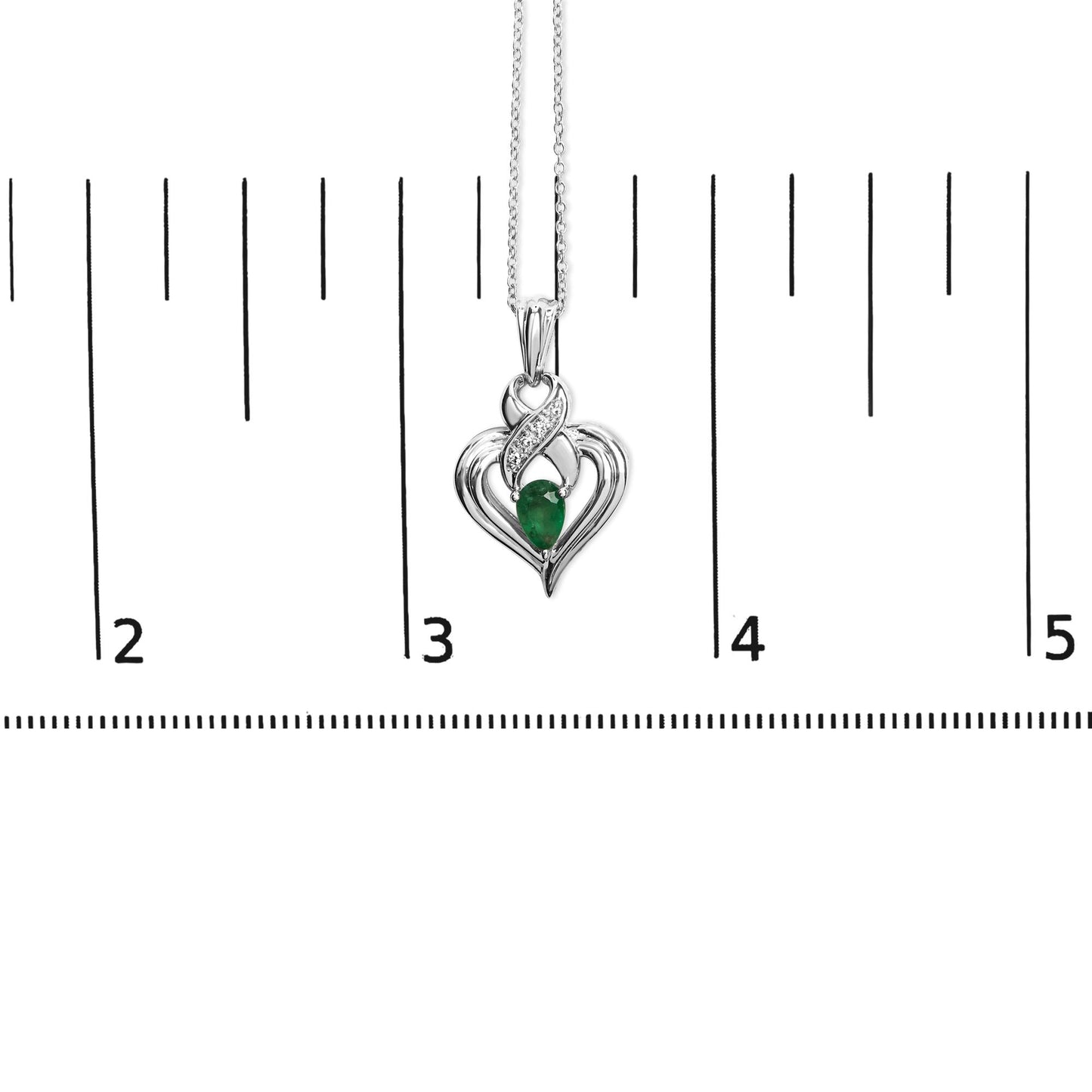 Close-up front view of a white metal heart-shaped necklace pendant with a pear-shaped green gemstone in the center and four round white gemstones above it, shown hanging on a chain against a ruler for size reference.