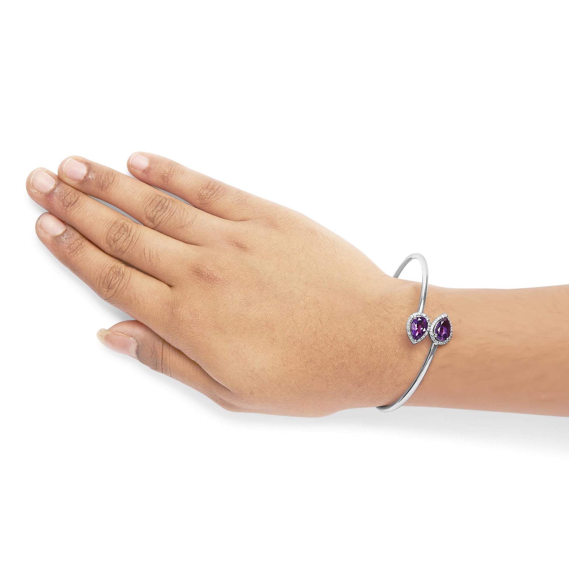 White metal open cuff bracelet with two pear-shaped purple gemstones surrounded by small white gemstones, shown on a model's wrist from a side angle.