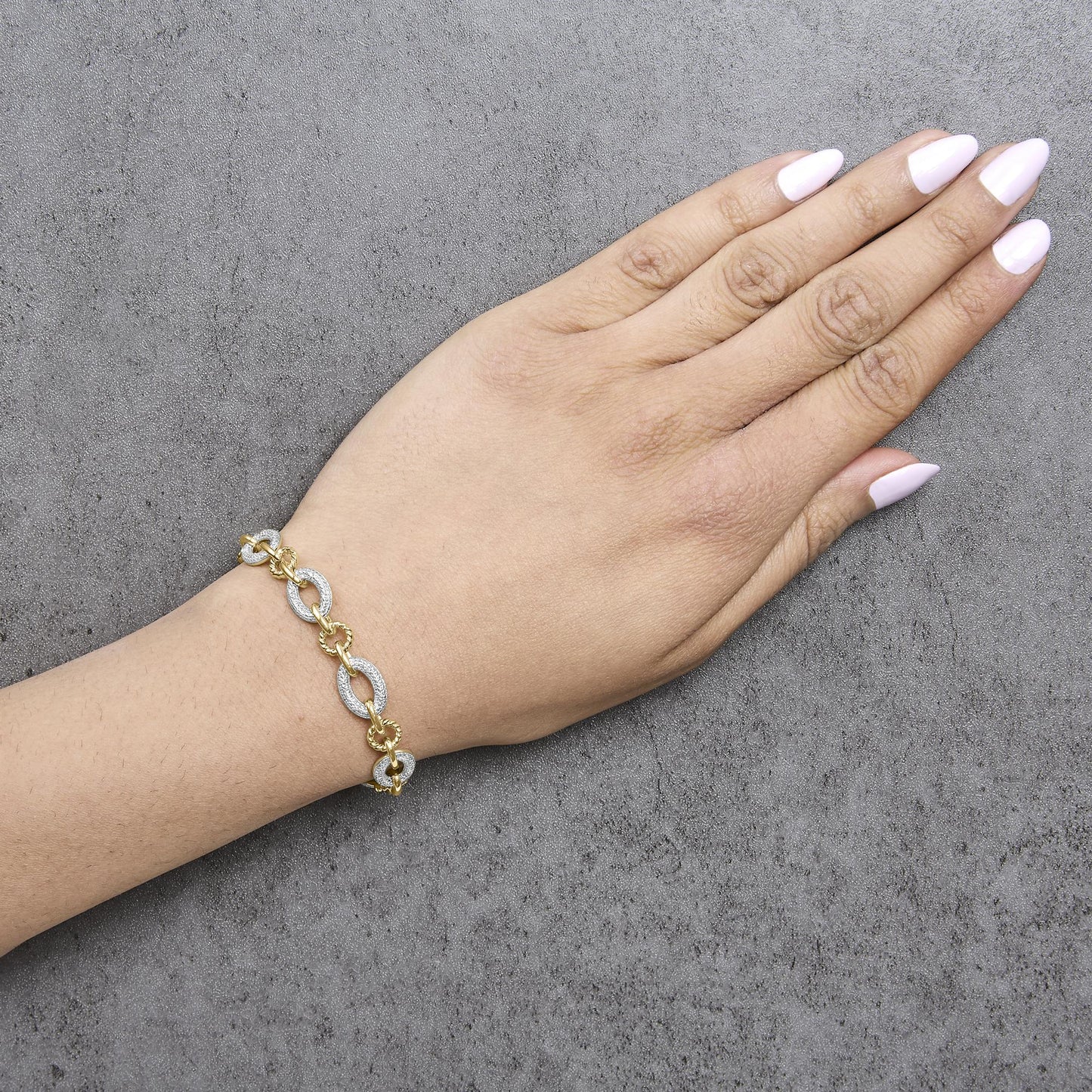 Yellow metal bracelet with alternating oval links featuring white gemstones in pave setting, shown worn on a model's wrist, top angle.