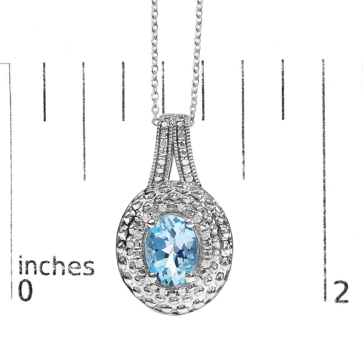Close-up front view of a white necklace pendant with a central oval blue gemstone surrounded by small round white gemstones in a pave setting, shown on a measurement scale.