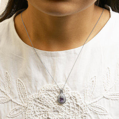 White metal necklace with a pear-shaped purple gemstone pendant surrounded by pave-set white round gemstones, shown worn on a model in a front close-up angle.