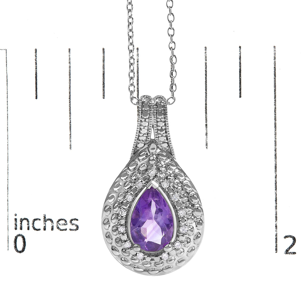 Close-up image of a white metal necklace pendant with a pear-shaped purple gemstone in the center, surrounded by small round white gemstones in a pave setting, shown on a scale.
