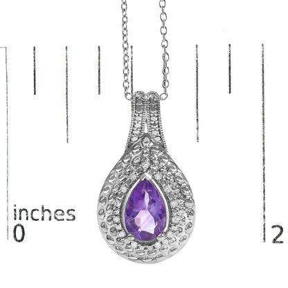 Close-up image of a white metal necklace pendant with a pear-shaped purple gemstone in the center, surrounded by small round white gemstones in a pave setting, shown on a scale.