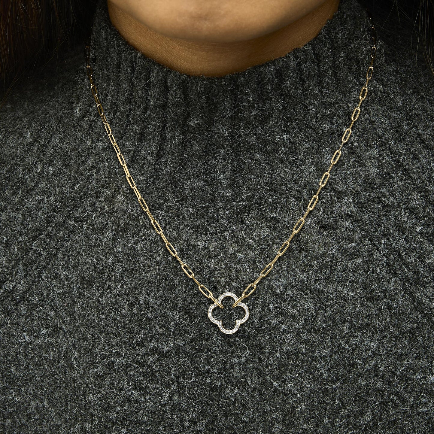 Close-up front view of a necklace worn on a model showing a yellow chain with a pendant featuring a quatrefoil shape paved with white gemstones.