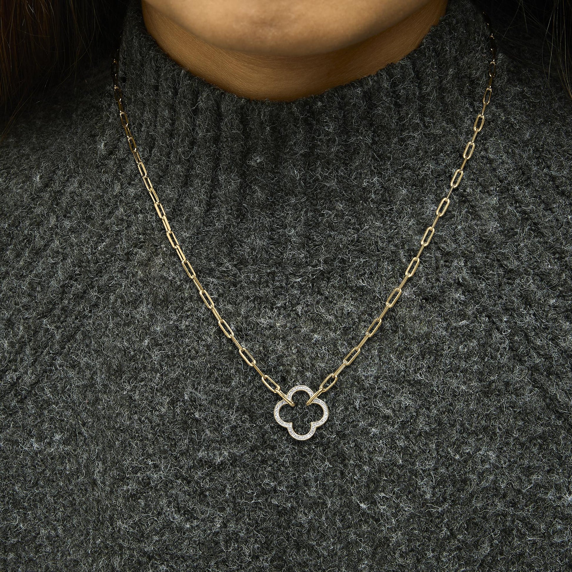 Close-up front view of a necklace worn on a model showing a yellow chain with a pendant featuring a quatrefoil shape paved with white gemstones.