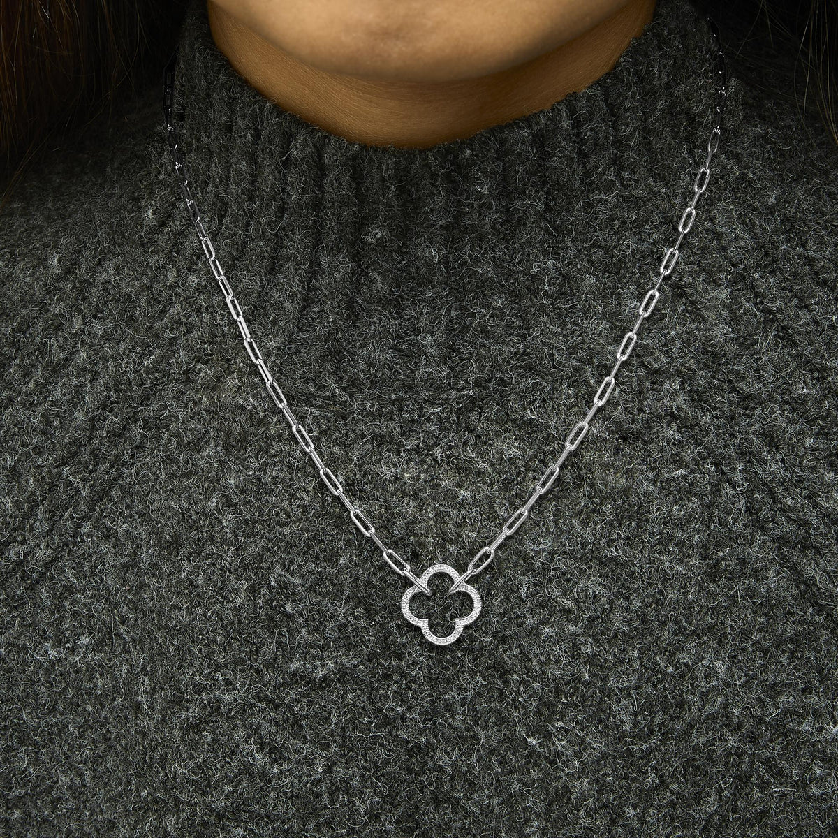White metal necklace with a clover-shaped pendant set with white gemstones in a pave setting, shown worn on a model from the front angle.