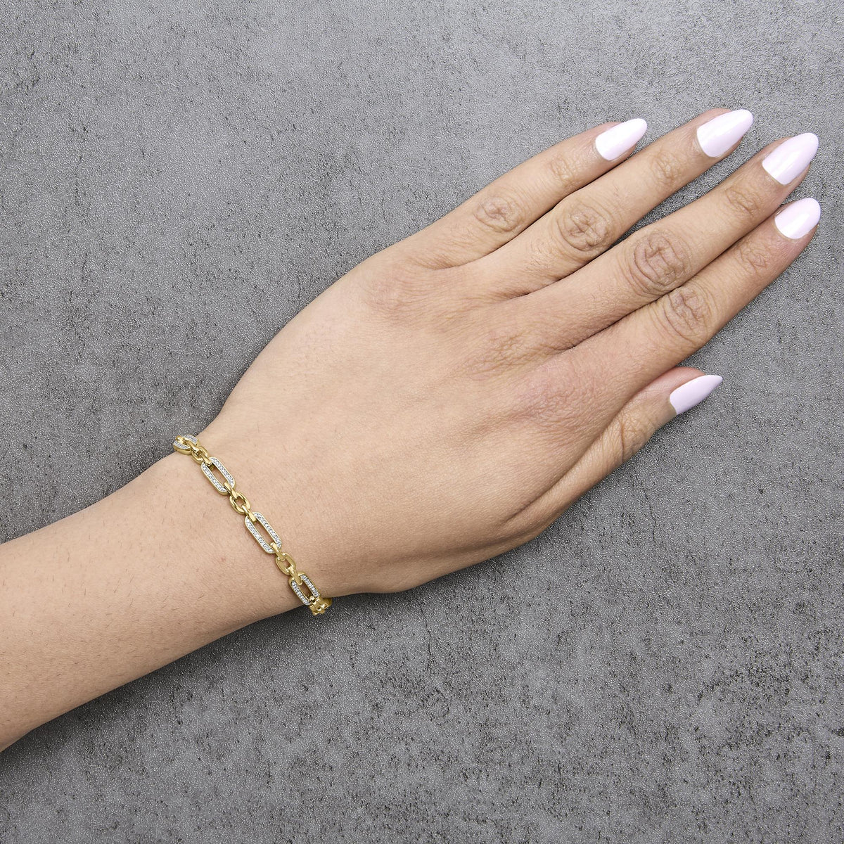 Close-up angled shot of a model's hand wearing a yellow metal bracelet with linked chain design, featuring links partially adorned with white gemstones in pave setting.