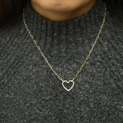 Close-up front view of a model wearing a yellow necklace with a heart-shaped pendant featuring white gemstones in a pave setting, on a textured dark gray sweater.